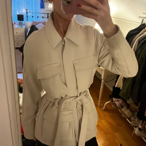 Beige kappa med bälte ifrån Gina - Säljer en superfin beige kappa i mycket bra skick. Den har långa ärmar och ett snyggt bälte i midjan som ger en elegant look. Perfekt för höst och vår! Passar både till vardags och lite finare tillfällen. Storleken är normal och den har praktiska fickor framtill. Den är ifrån Gina🥰
