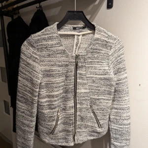 Gråmelerad cardigan från Gina Tricot - Säljer en snygg gråmelerad cardigan från Gina Tricot i storlek S. Jackan har en dragkedja framtill och två fickor med dragkedjor.