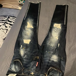 Mörkblå jeans från Dsquared2 - Säljer ett par snygga mörkblå jeans från Dsquared2. De har en cool distressed look med slitningar och färgstänk. Perfekta för en avslappnad stil! Jeansen har en normal passform och är i bra skick. Passar perfekt till både vardag och fest. Ny pris 6080 kr