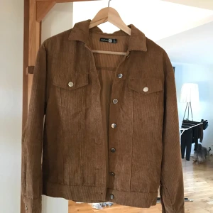 Brun manchesterjacka från Boohoo - Säljer en snygg brun manchesterjacka från Boohoo. Jackan har en klassisk krage och knappar framtill. Den är i mycket bra skick och perfekt för höst och vår. Storleken är dam M och den har långa ärmar. Perfekt för en casual look!