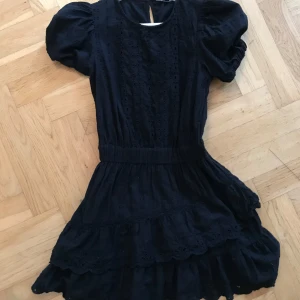 Svart klänning med volangdetaljer - Love shack fancy liknande svart volang klänning med korta puffärmar och vackra volangdetaljer. Klänningen har en broderad design och en smickrande passform med elastisk midja