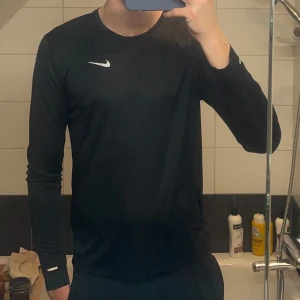 Svart långärmad tröja från Nike - Säljer nu denna snygga svarta träningströja från Nike, har ett Nike märke på ena bröstet. Skönt och bra material till träning!! Skriv vid frågor