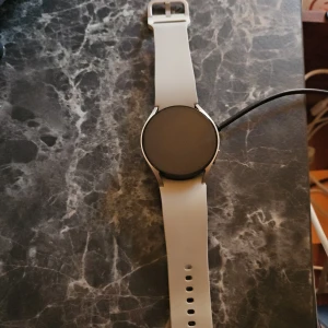 Vit smartklocka med laddare - Samsung smartwatch 6 Säljer en stilren vit smartklocka med rund urtavla och matchande armband. Perfekt för den teknikintresserade som vill hålla koll på sin hälsa och notifikationer. Laddare medföljer.använd 6 månader kvitto finns ,garanti