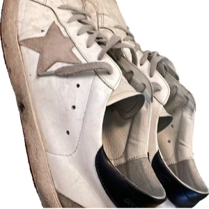 Vita golden goose skor - Säljer ett par vita golden goose skor med en cool stjärndetalj på sidan. Skorna har snörning och en lite sliten look som ger dem en avslappnad stil. Perfekta för vardagsbruk och passar till nästan allt. De har en bekväm passform och är i bra skick.