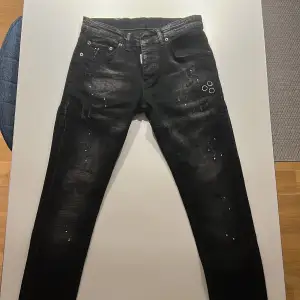 Säljer ett par svarta jeans från Dsquared2 i storlek 42. De har en cool distressed look med färgstänk och slitningar. Perfekta för en avslappnad men stilren outfit. Tillverkade i Italien med hög kvalitet. Passar både till vardags och fest!