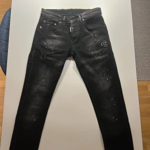 Svarta jeans från Dsquared2 - Säljer ett par svarta jeans från Dsquared2 i storlek 42. De har en cool distressed look med färgstänk och slitningar. Perfekta för en avslappnad men stilren outfit. Tillverkade i Italien med hög kvalitet. Passar både till vardags och fest!