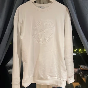 Vit sweatshirt från Stone Island - Säljer en stilren vit sweatshirt från Stone Island med ett diskret broderat emblem på bröstet och det klassiska märket på ärmen.    Köpte tröjan för 2700kr nästan aldrig andvänd som ny. Tröjan är i storlek xl men är jätte liten är storleken jag är 177 och har storlek s och den passar mig perfekt så mellan s och xl 