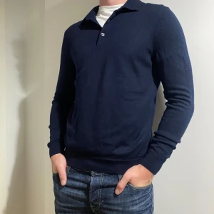 Mörkblå merinoull långärmad piké - Säljer en stilren mörkblå tröja med krage och knappar. Perfekt för både vardag och fest. Tröjan har långa ärmar och är gjord i ett mjukt material som känns skönt mot huden. 