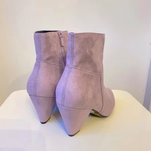 Ljuslila boots med klack - Säljer ett par snygga ljuslila boots i mocka med spetsig tå och klack. De har en dragkedja på sidan för enkel på- och avtagning. Perfekta för både vardag och fest! 🥰