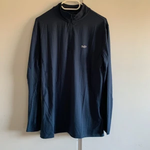 Svart långärmad tröja från MP - Säljer en stilren svart långärmad tröja från MP. Perfekt för träning eller vardagsbruk. Tröjan har en halv dragkedja framtill och är i nyskick, fortfarande i originalförpackning. Passar bra till höst och vår. Skön och funktionell design!