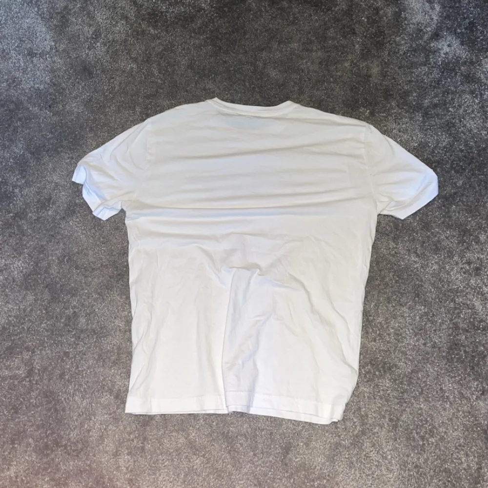 Säljer en snygg vit t-shirt från Emporio Armani med deras ikoniska logga i blått och svart på framsidan. T-shirten är kortärmad och perfekt för en casual look. Passar bra till både jeans och shorts. Perfekt för sommaren! 🌞. T-shirts.