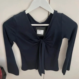 Mörkblå topp med knytning - Snygg mörkblå topp i storlekXS med lång ärm och knytning framtill. Perfekt för både vardag och festliga tillfällen. Toppen har en figurnära passform och är gjord i ett mjukt och bekvämt material. oops lappen är inte kvar❤️