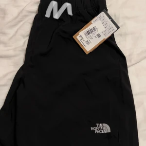 Svarta shorts från The North Face - Säljer ett par svarta shorts/badshorts från The North Face i storlek M. Perfekta för utomhusaktiviteter med en bekväm passform och elastisk midja. Byxorna är i nyskick och har en stilren design med logotypen på benet. Oanvända med tagg på. Köptes för (350 dkk) på jd sports.
