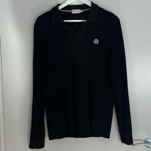 Moncler Piké Tröja - Moncler Svart Piké Tröja. I bra utan defekt. Storlek S. Nypris är runt 2900 kr. Skickar alltid samma dag eller nästa dag. Skriv för mer information eller frågor.