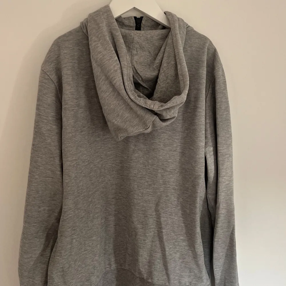 Säljer en stilren grå hoodie i mjukt material med dragkedja framtill. Perfekt för både höst och vår. Den har en bekväm passform och praktiska fickor. Huvan har svarta snören för justering. Perfekt för en avslappnad look!. Neuletakit & Villapaidat.