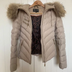 Hollies jacka - Fin beige kort vinterjacka från Hollies med päls på luvan som går att ta av! Leopardmönstrad inuti. Storlek 32 men passar större också, köpt för 4000kr. Säljer då den inte kommer till användning mer. Säljer en likadan i svart. 