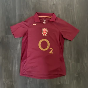 Arsenal tröja - Denna t shirten är retro och är en arsenal tröja från 03-04. Spelaren på ryggen är Henry N14 och den är helt äkta. Köpt för 1100 säljs för betydligt mycket billigare 399 kr🔥