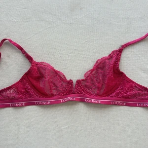 Rosa spets-BH från Lounge - Säljer en superfin rosa spets-BH från Lounge. Den har en elegant spetsdesign och justerbara axelband. Perfekt för att känna sig både bekväm och snygg. Resårbandet har Lounge-loggan tryckt runtom. Passar perfekt till vardags eller speciella tillfällen. 💖