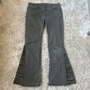 Lågmidjade gråa jeans bootcut - Säljer dessa gråa lågmidjade jeans med slitningar och zebra-slits. Midjemått: 41cm Innebenslängd: 78cm. De är för stora på mig som vanligtvis bär XS eller 25 i jeans. Har du någon fråga är det bara att höra av dig🫶🏻