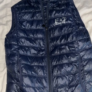 Armani EA7 väst - Säljer min mörkblå Armani väst då den är lite för liten för mig, västen är i väldigt bra skick men de finns ett litet hål längst ner på baksidan som man inte märker. Västen är storlek M men är lite liten i storleken så den passar bra på både M och S