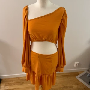 Orange oneshoulder klänning från NA-KD - Säljer en superfin orange oneshoulder klänning från NA-KD. Den har långa ärmar och en snygg volangdetalj på kjolen. Perfekt för en sommarfest eller en utekväll! Klänningen är i nyskick och har en tight passform som framhäver figuren.