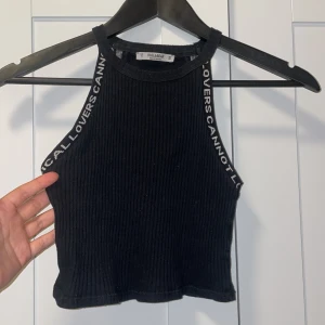Svart ribbad topp från Pull&Bear - Säljer en svart ribbad topp från Pull&Bear. Den är ärmlös och har en cool text längs axelbanden som säger 'RADICAL LOVERS CANNOT LOSE'. Perfekt för en avslappnad sommarlook eller en utekväll. Toppen är i bra skick och superbekväm!