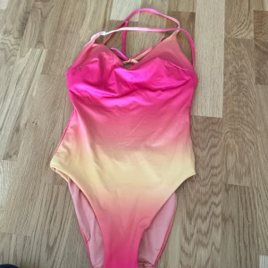 Färgglad baddräkt från Index - Säljer en superfin baddräkt från Lindex i storlek xs. Den har en snygg ombre-effekt i rosa och gul som verkligen poppar! Baddräkten är gjord av återvunnen polyester och har en bekväm passform. Perfekt för sommarens alla badäventyr! 🌞
