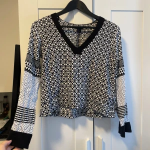 Svartvit mönstrad tröja från H&M - Säljer en snygg svartvit mönstrad tröja från H&M. Den har en v-ringad hals och långa ärmar med olika geometriska mönster. Perfekt för både vardag och fest!