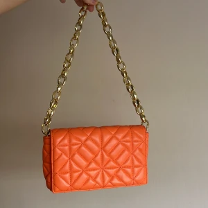 Orange quiltad axelväska med kedja - Snygg orange axelväska med quiltat mönster och en elegant guldkedja som axelrem. Väskan har en praktisk ficka inuti för säker förvaring. Perfekt för att ge en färgklick till din outfit!