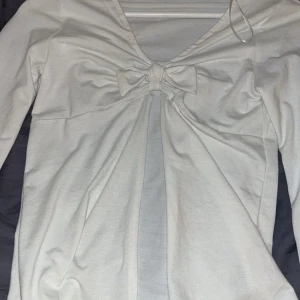 Vit långärmad topp med rosett - Säljer en stilren vit långärmad topp med en söt rosett framtill med utsvängda armar. Den är ifrån h&m från barn avdelningen i storlek 170 sitter bra på någon med storlek xs/s den är i fint skick o inga fläckar eller hål 