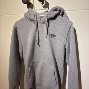 Alpha industries hoodie - Säljer en grå hoodie från Alpha iIndustries i storlek S och är i mycket bra skick förutom att ena ringen till snöret har gått sönder men annars så är den i väldigt bra skick.