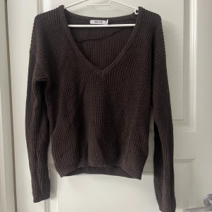 Brun stickad tröja från NA-KD - Säljer en snygg brun stickad tröja från NA-KD med v-ringning. Tröjan har långa ärmar och en bekväm passform, perfekt för kyligare dagar. Ett måste i garderoben för en stilren look.