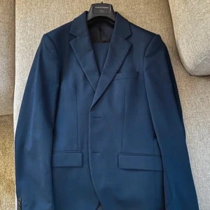 Mörkblå kavaj från Tiger of Sweden - Snygg mörkblå kavaj från Tiger of Sweden. Klassisk design med knappar fram och på ärmarna. Sjukt bra skick och använd fåtal tillfällen. Byxor storlek 48 och kavaj 44. Jag ska köpa nytt set men levla upp en storlek i kavajen därav den säljs!
