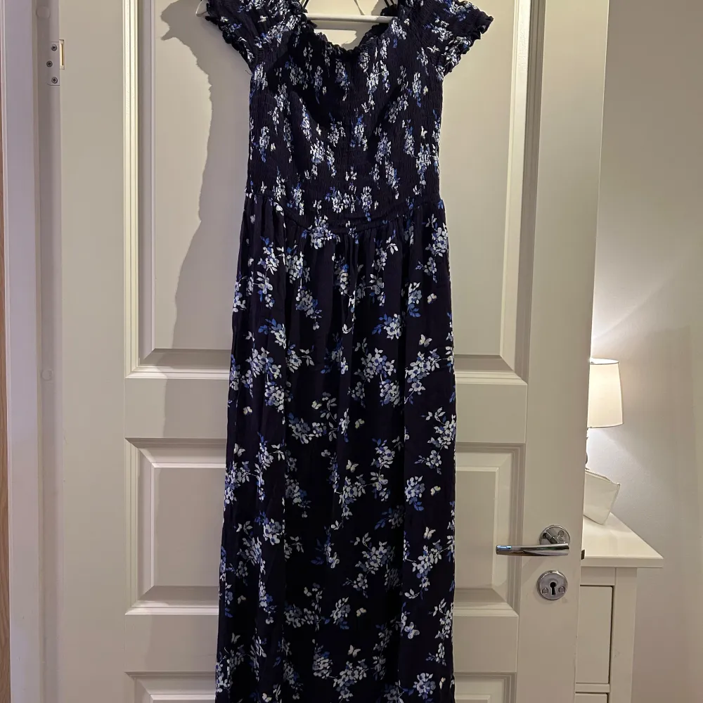 Säljer en vacker långklänning med blommigt mönster i blått och vitt. Klänningen har offshoulder-ärmar och volangdetaljer vid axlarna. Perfekt för sommarens festligheter!. Mekot.