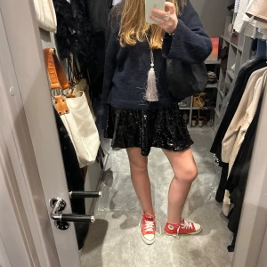 Svart glittrig kjol - Snygg svart glittrig kjol som passar perfekt för en kväll ute. Kjolen har en kort längd och är täckt med paljetter som ger en extra touch av glamour. Perfekt för att sticka ut och glänsa!