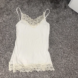 Vit spetslinne från Gina Tricot - Säljer ett stilrent vitt linne från Gina Tricot i storlek XS. Linnet har smala axelband och vacker spetsdetalj vid halsringning och nederkant. Perfekt för att lägga till en liten snygg toutch i slutet av tröjan tex!