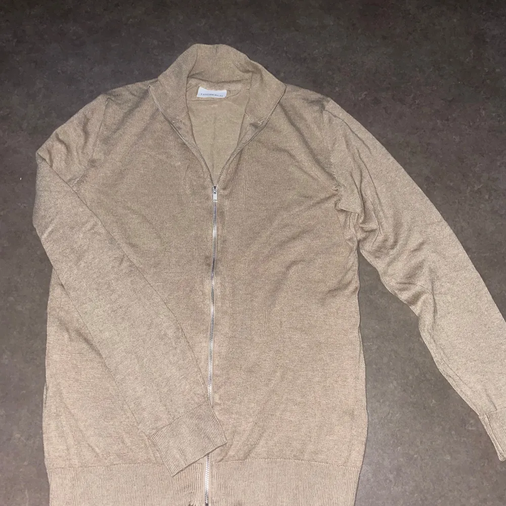 Säljer en stilren beige kofta från Lindbergh med dragkedja framtill. Koftan har långa ärmar och en ribbad krage samt muddar vid ärmslut och nederkant. Perfekt för en avslappnad och snygg look, slim fit modell. Tröjan är helt ny aldrig andvänd, men prislappen är borttagen🙌.. Neuletakit & Villapaidat.
