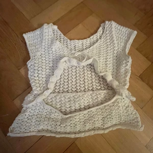 Vit virkad topp - Charmig vit virkad topp med korta ärmar och en öppen ryggdetalj. Toppen har en söt volangkant och knytning baktill. Perfekt för varma sommardagar. Storleken står inte, men skulle säga att den passar som en xs! 