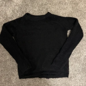 Svart stickad tröja - Säljer en mysig svart stickad tröja med långa ärmar. Perfekt för kyliga dagar och enkel att matcha med olika outfits. Tröjan har en klassisk design med ribbstickade muddar vid ärmslut och nederkant.