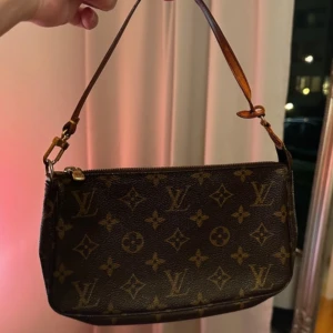 Brun monogram axelväska från Louis Vuitton - Intressekoll på min älskade lv pochette med det klassiska monogrammönstret. Väskan har en dragkedja upptill och en justerbar axelrem i läder.  Verkligen så snygg och passar till allt!! Har reparerat en skada hos skomakare också så den är i bra skick!