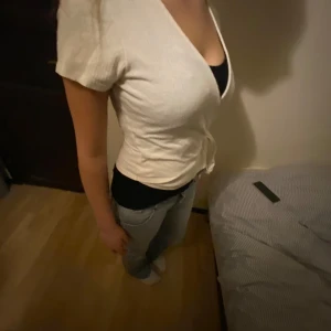 Vit omlottopp med knytband - Säljer en stilren vit omlottopp med korta ärmar och knytband i sidan. Toppen har en v-ringad design och är perfekt för en avslappnad look. Den är gjord i ett mjukt material som ger en bekväm passform. Står ingen storlek men uppskattas till s-m. Modellen bör vandlugtvis s 