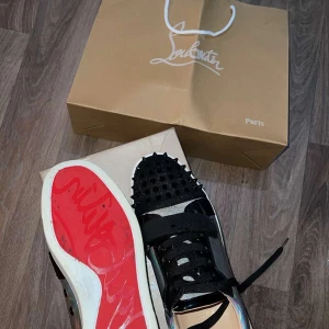  Louboutin Skor - Snygga sneakers med holografisk yta och svarta detaljer från Louboutin. Skorna har en röd sula och är dekorerade med nitar på tån. Perfekta för att sticka ut med en unik stil.