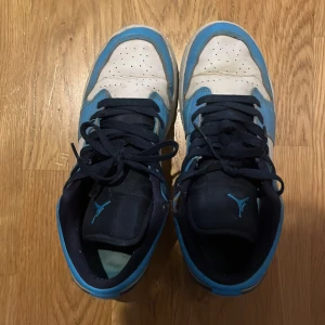 Nike Air Jordans i blått och vitt - Säljer ett par Nike Air Jordans i blått och vitt med svarta detaljer. Skorna har snörning och en klassisk Nike-logga på sidan. Perfekta för sneaker-entusiaster!