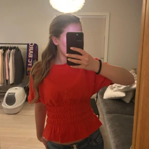 Röd topp med resårmidja - Säljer en snygg röd topp med resår i midjan som ger en fin passform. Toppen har korta ärmar och en rund halsringning. Perfekt för att liva upp garderoben!