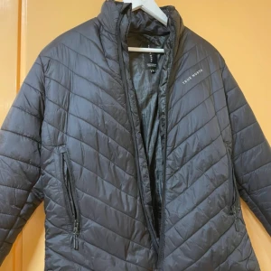 Svart pufferjacka från True North - Säljer en svart pufferjacka från True North. Jackan har en dragkedja framtill och två sidofickor med dragkedjor. Perfekt för kyliga dagar med sin quiltade design som håller värmen. En stilren och funktionell jacka för alla tillfällen.