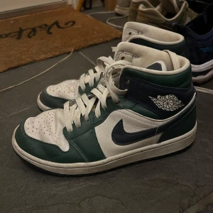 Nike Air Jordans i grönt och vitt - Snygga Nike Air Jordans i grönt och vitt med klassisk snörning. Skorna har en hög design med det ikoniska Air Jordan-märket på sidan. Perfekta för dig som vill ha en stilren och sportig look.