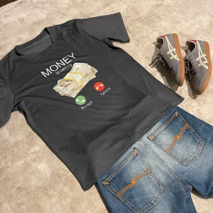 Money is calling FET tisha - Cool svart t-shirt med ett humoristiskt tryck av en bunt pengar och texten 'MONEY is calling'. Perfekt för en avslappnad stil.