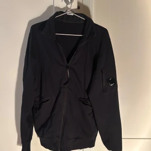 Svart zip tröja från C.P. Company - Säljer en svart zip från C.P. Company med dragkedja, Perfekt för en stilren look. Väldigt bra skick, i storlek M.
