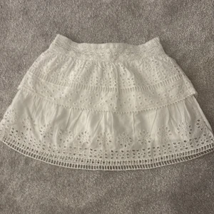 Vit kjol från Zara - Charmig vit kjol från Zara med broderade detaljer och volanger. Perfekt för varma dagar med sin luftiga design och elastiska midja för extra komfort.