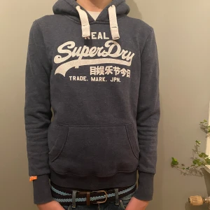 Mörkblå hoodie från SuperDry - Säljer en snygg mörkblå hoodie från SuperDry med vit text på bröstet. Storlek: M Skick: 8/10 Texten är tyvärr lite dåligt skick, men inget man inte kan fixa! Skriv gärna vid intresse!